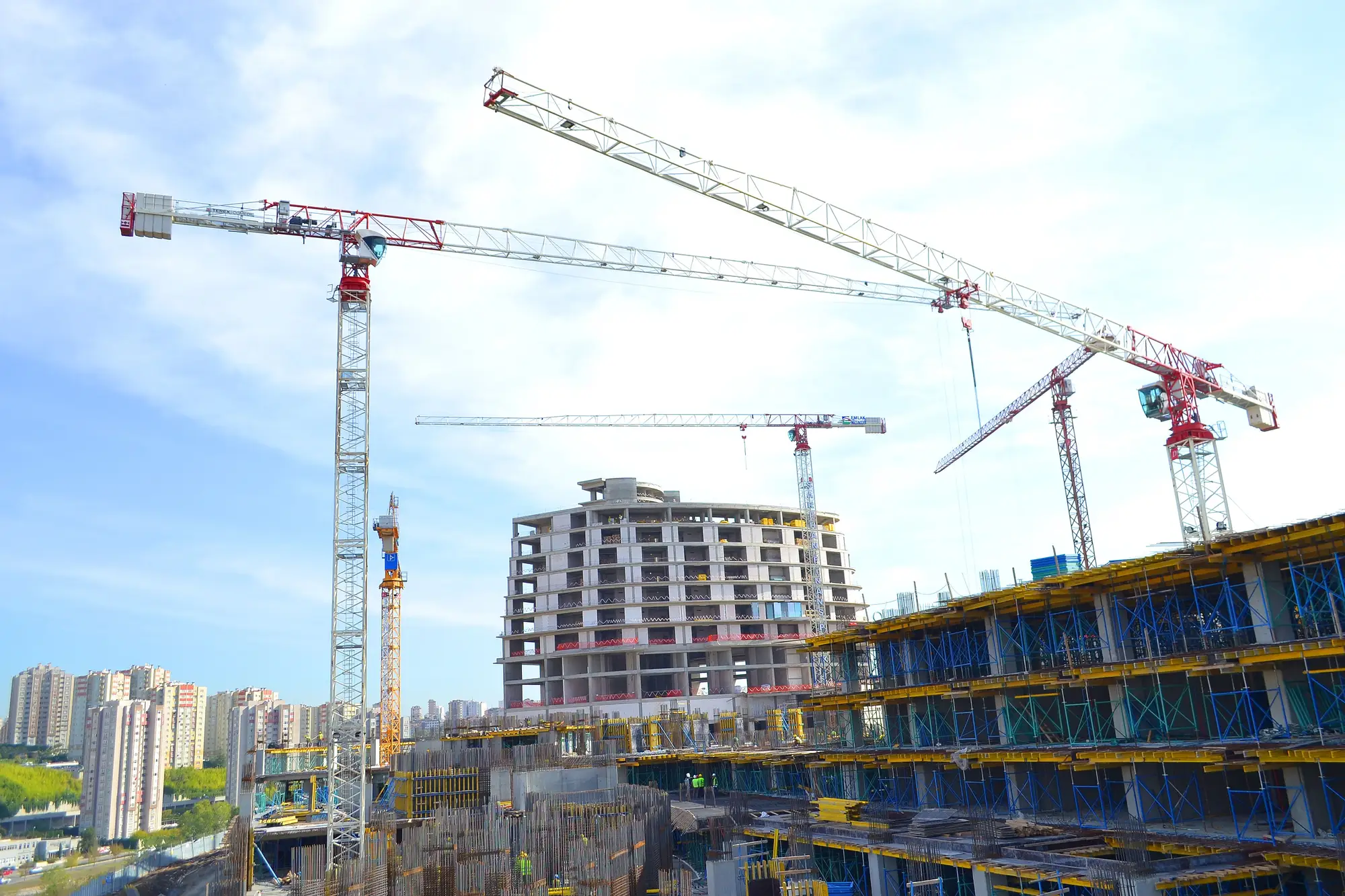 Tower cranes over a concrete frame rising beside a topped-out residential block